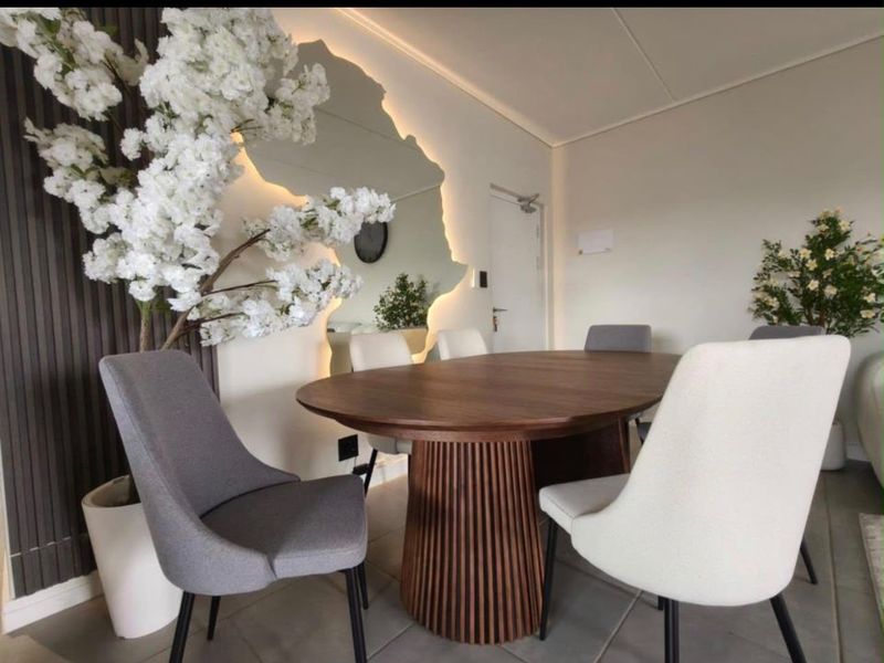 A modern dining area featuring stylish slatted wood wall paneling, a unique backlit mirror, and neutral tiled flooring.