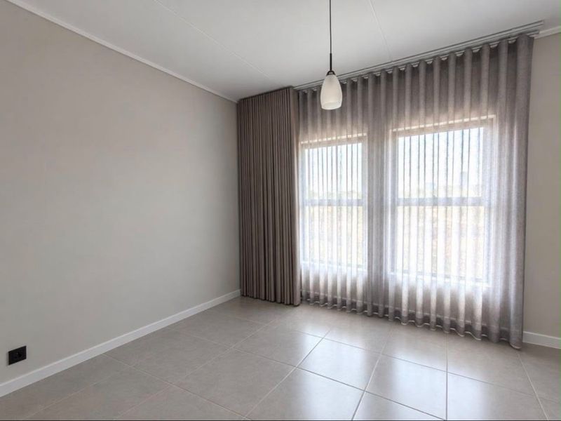 A bright, empty bedroom featuring neutral tiled flooring, modern pendant lighting, and floor-to-ceiling curtain tracks, offering a clean and versatile living space.