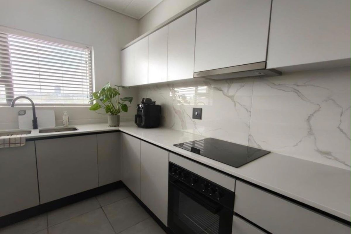 Modern kitchen featuring sleek handleless cabinetry, stone countertops, marble-look splashback, integrated electric hob, oven, and extractor fan with tiled flooring.