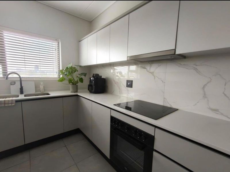 Modern kitchen featuring sleek handleless cabinetry, stone countertops, marble-look splashback, integrated electric hob, oven, and extractor fan with tiled flooring.