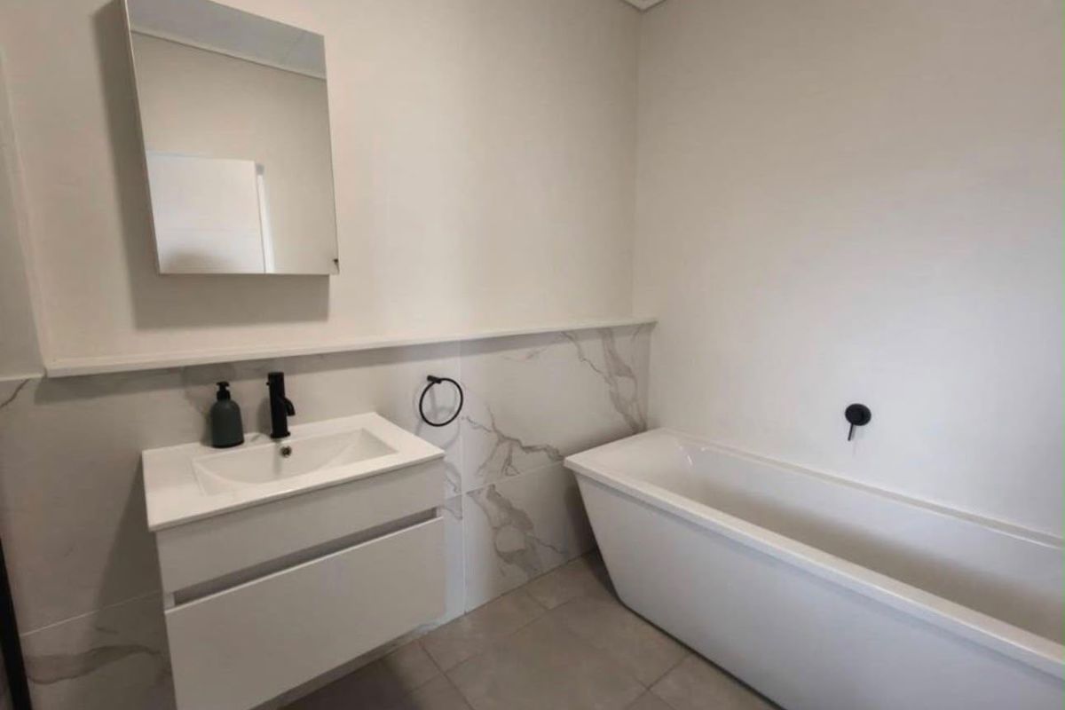 Modern bathroom featuring a sleek wall-mounted vanity, a contemporary freestanding bathtub, and elegant marble-look wall tiling with matte black fixtures.