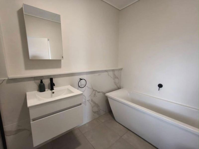 Modern bathroom featuring a sleek wall-mounted vanity, a contemporary freestanding bathtub, and elegant marble-look wall tiling with matte black fixtures.