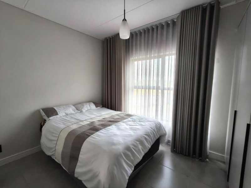 A well-maintained bedroom featuring neutral wall tones, tiled flooring, a built-in wardrobe, and floor-to-ceiling curtains providing natural light.