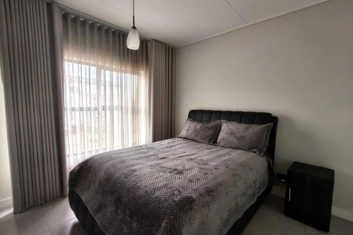 A well-maintained bedroom featuring neutral wall tones, tiled flooring, and floor-to-ceiling curtains that provide ample natural light.