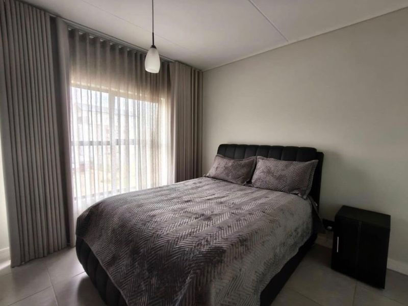 A well-maintained bedroom featuring neutral wall tones, tiled flooring, and floor-to-ceiling curtains that provide ample natural light.
