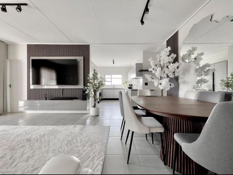 Modern open-plan living and dining area featuring contemporary slatted wood wall accents, sleek tiled flooring, and a seamless transition into a well-appointed kitchen.