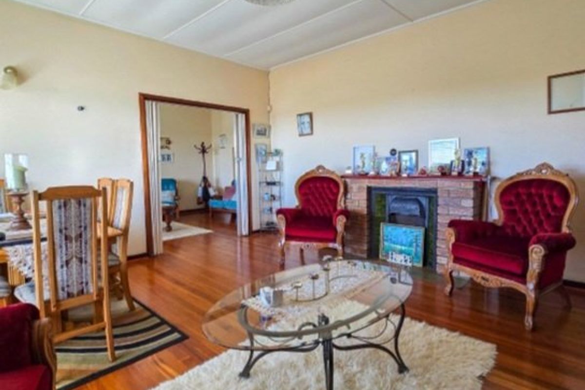 A spacious living room featuring polished hardwood flooring, a classic brick fireplace, and a ceiling fan, with an adjacent room visible through sliding doors.
