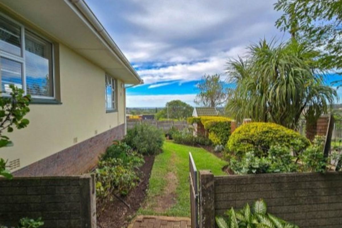 A view of the rear garden featuring a brick pathway, established landscaping, and a brick boundary wall alongside the side elevation of the house.