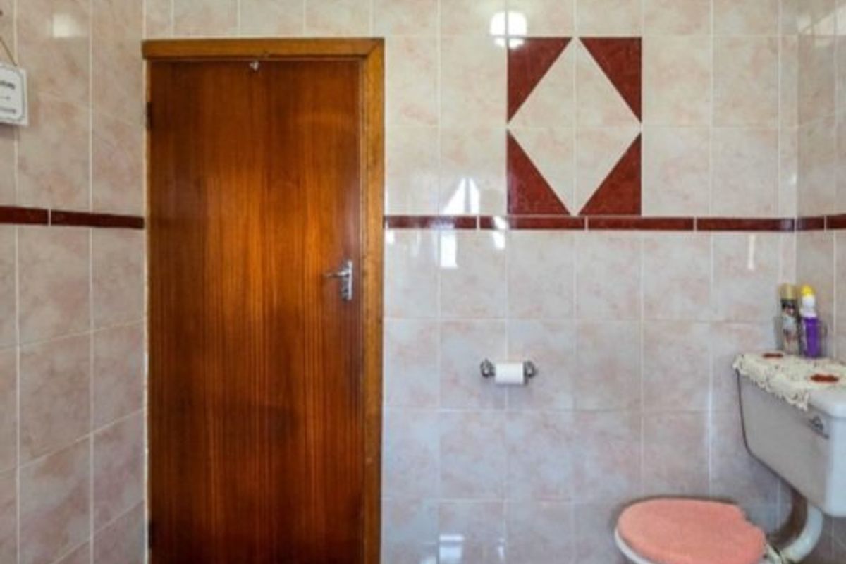 A functional bathroom featuring full-height ceramic wall tiling with decorative accents, tiled flooring, and a standard toilet suite.