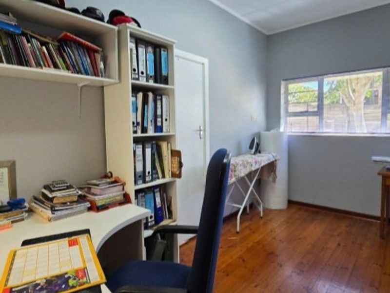 A functional home office space featuring warm hardwood flooring, neutral wall tones, and natural light through an aluminium-framed window.