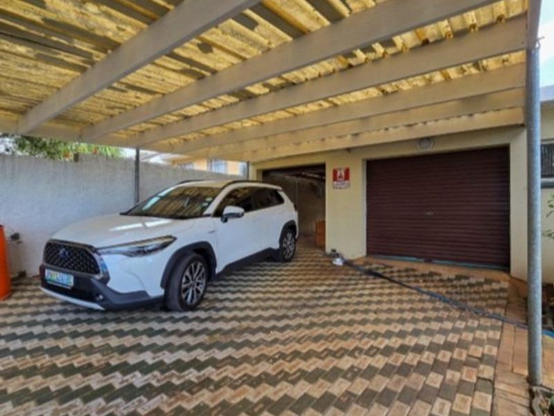 A covered carport area featuring paved flooring and a secure roller shutter garage door, providing sheltered parking space.