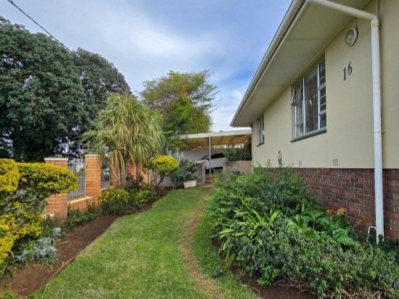 A view of the rear exterior of the house featuring a brick and plaster facade, a carport, and a landscaped garden area.