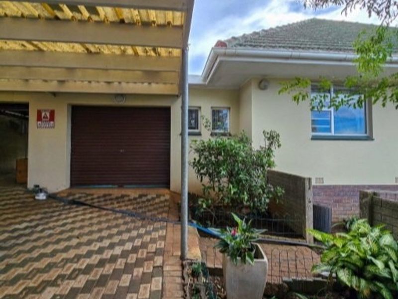 Front exterior view featuring a paved driveway, covered carport, and single garage entrance with a tiled roof structure.