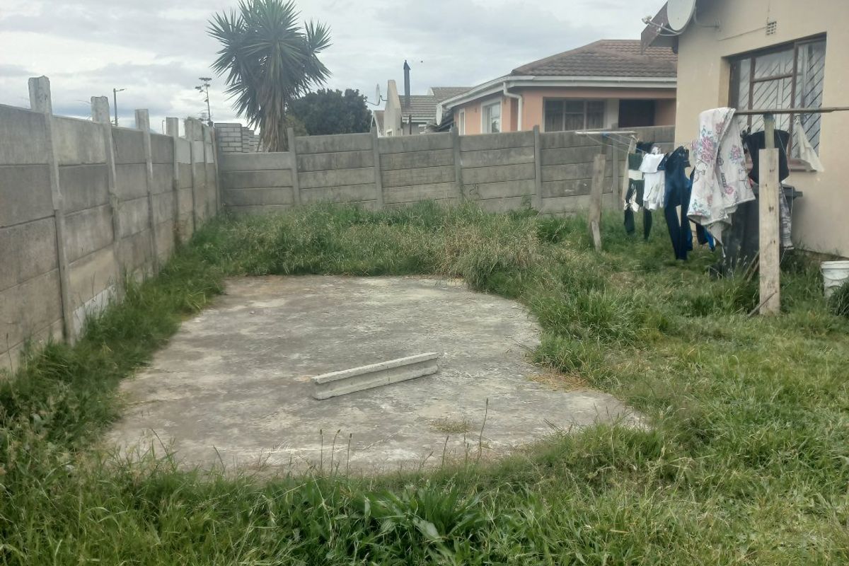Rear garden area featuring a concrete slab, precast boundary walling, and exterior wall access, currently requiring landscaping and maintenance.