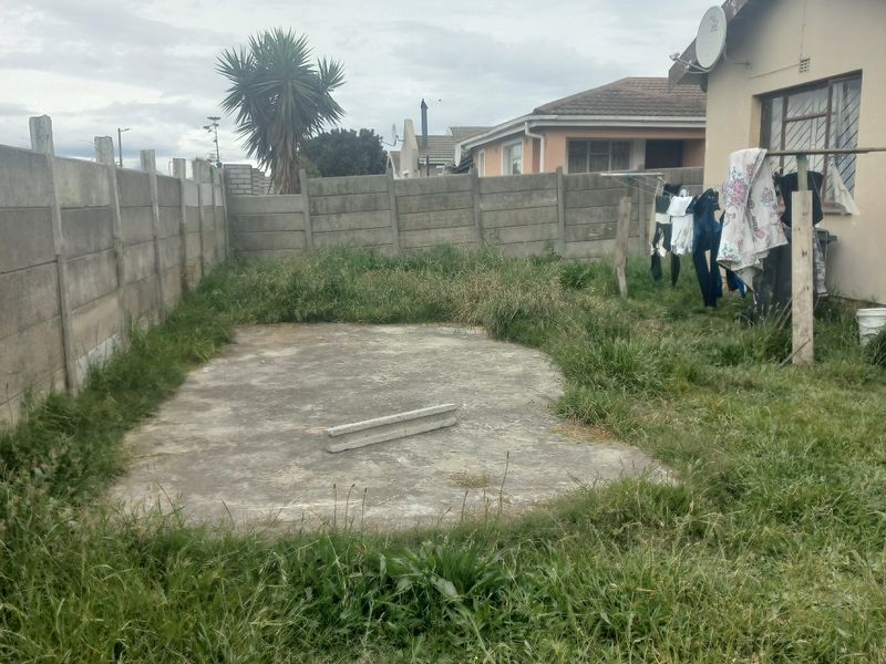 Rear garden area featuring a concrete slab, precast boundary walling, and exterior wall access, currently requiring landscaping and maintenance.