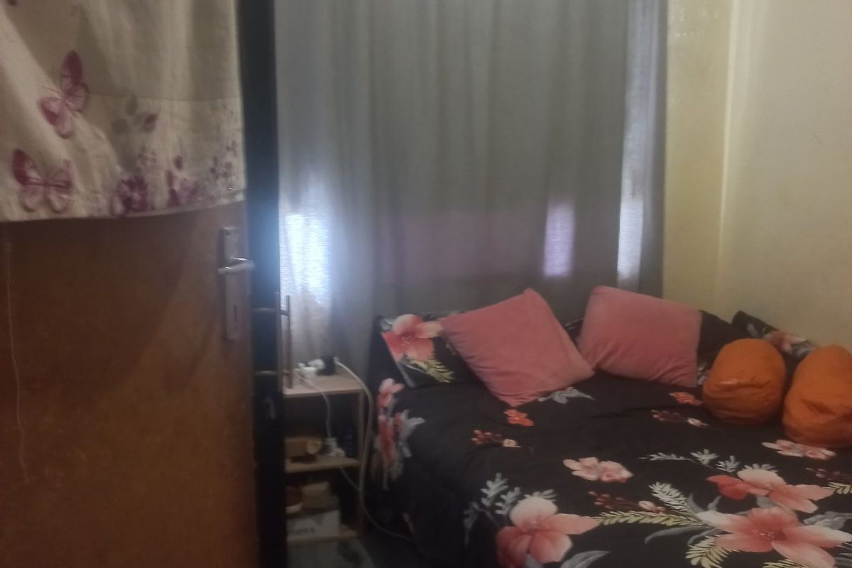 A compact bedroom featuring a window with curtains and visible signs of wear on the ceiling and walls.