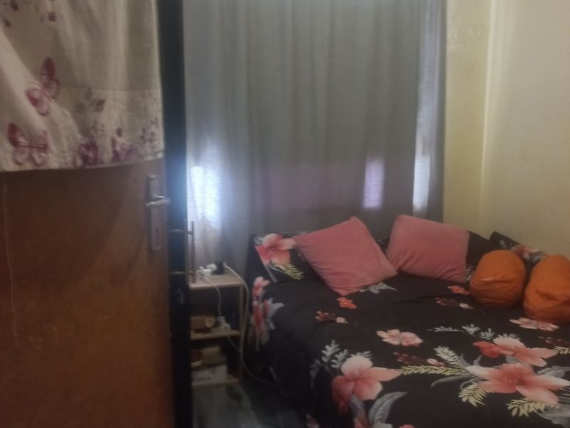 A compact bedroom featuring a window with curtains and visible signs of wear on the ceiling and walls.