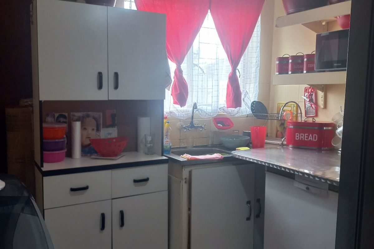 A compact kitchen featuring white cabinetry, a stainless steel countertop, and tiled flooring, offering a functional layout in need of cosmetic updates.