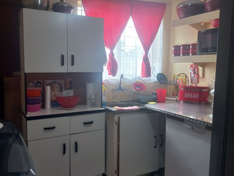 A compact kitchen featuring white cabinetry, a stainless steel countertop, and tiled flooring, offering a functional layout in need of cosmetic updates.