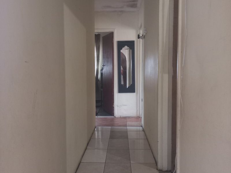 A narrow residential hallway featuring tiled flooring, showing signs of ceiling water damage and exposed electrical wiring requiring maintenance.