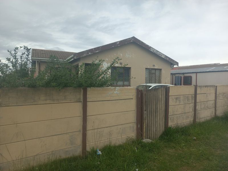 Front view of a single-story house featuring a precast concrete boundary wall, timber gate, and tiled roof, showing signs of exterior wear.