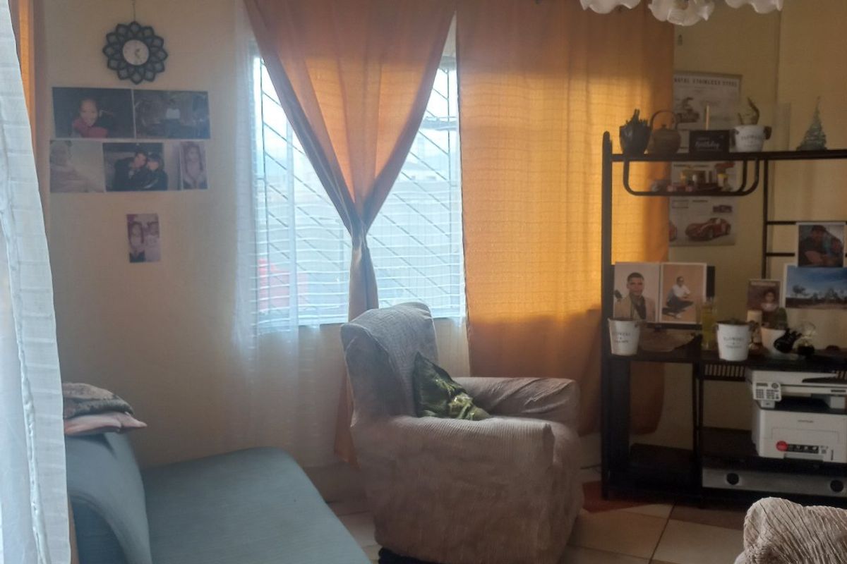 A living room featuring tiled flooring, a decorative ceiling light fixture, and a window fitted with security bars.