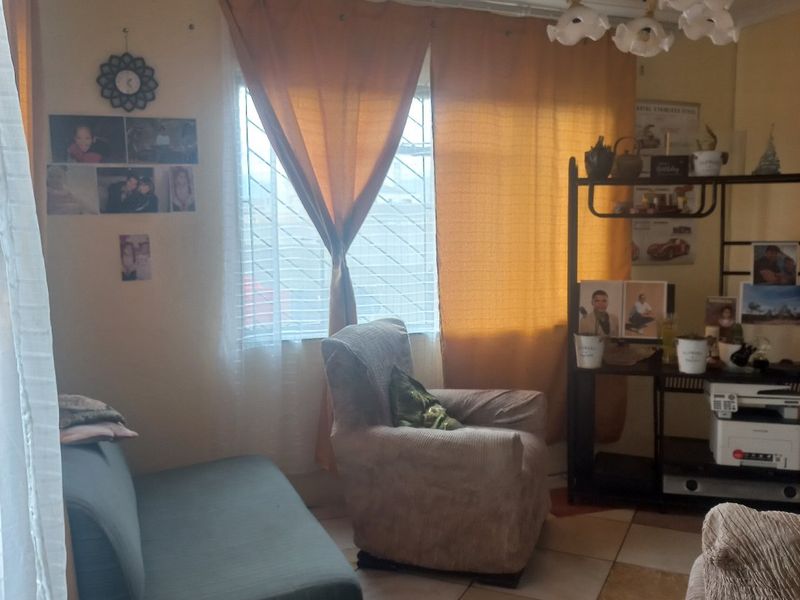 A living room featuring tiled flooring, a decorative ceiling light fixture, and a window fitted with security bars.