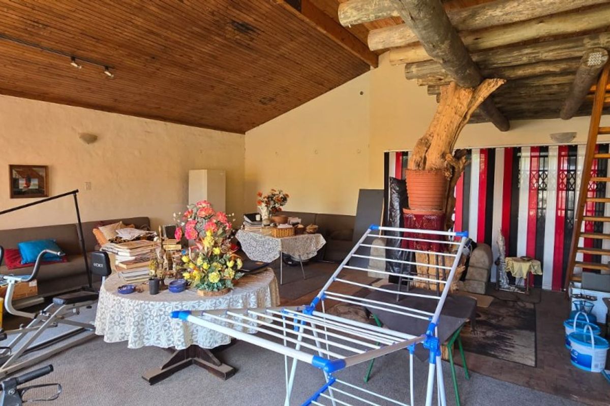 Spacious living area featuring a high exposed timber ceiling, rustic log support beam, and a wooden staircase leading to an upper level.