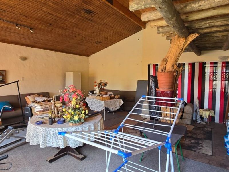 Spacious living area featuring a high exposed timber ceiling, rustic log support beam, and a wooden staircase leading to an upper level.