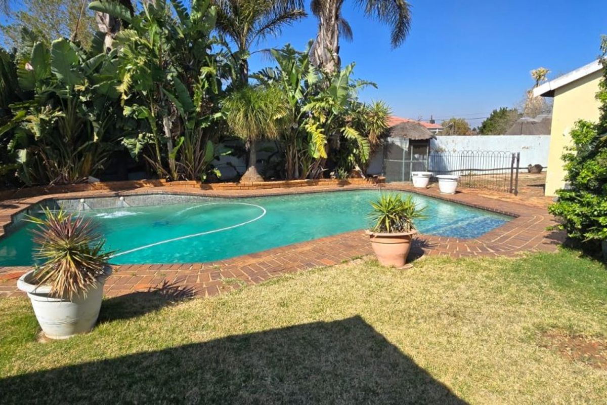 A private outdoor swimming pool area featuring brick coping, established garden landscaping, and perimeter walling.