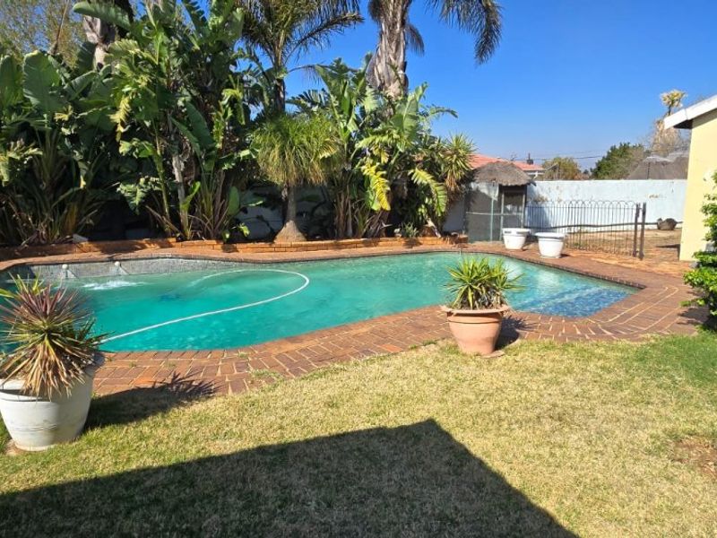 A private outdoor swimming pool area featuring brick coping, established garden landscaping, and perimeter walling.
