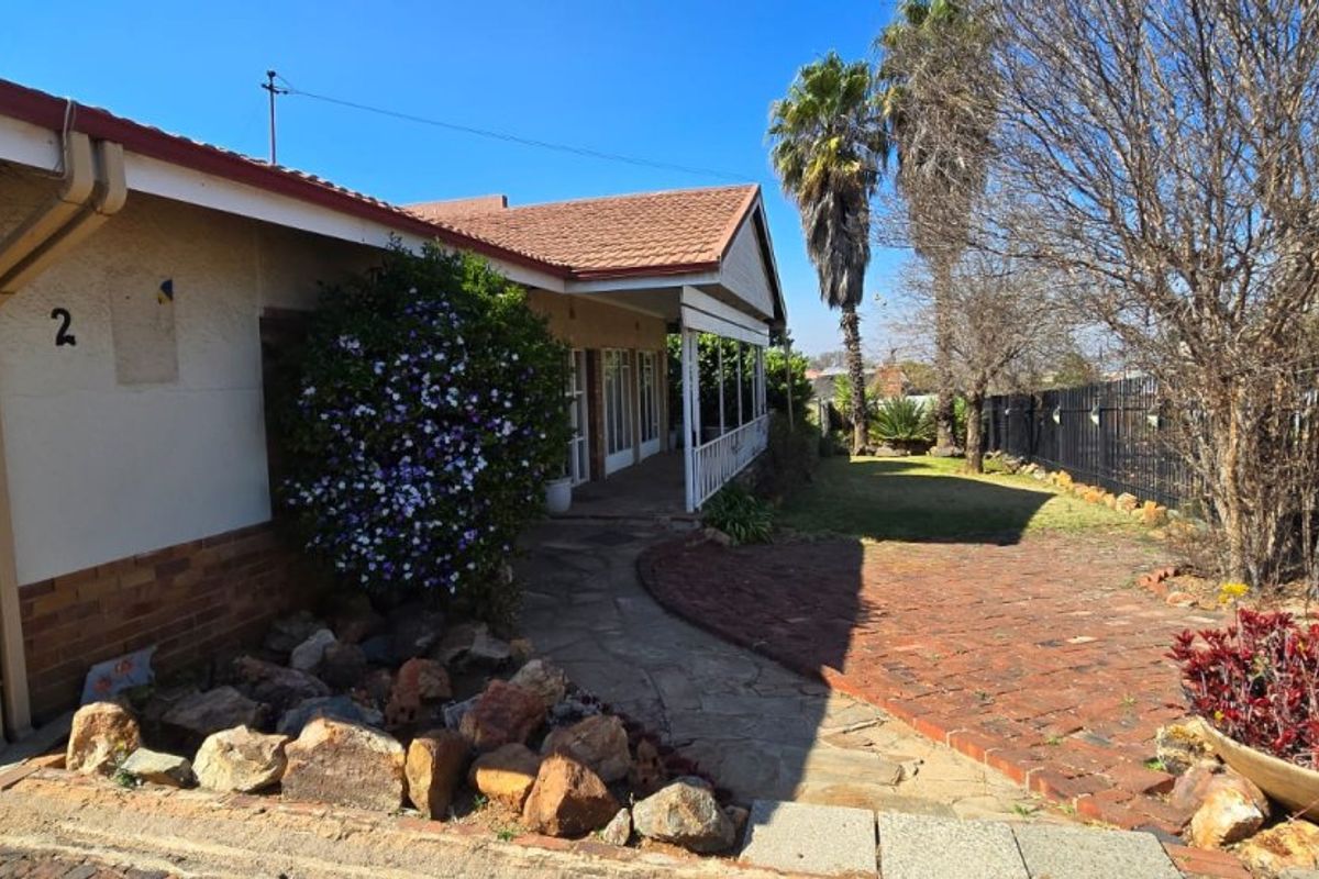Front elevation of a residential property featuring a covered veranda, brick paved pathway, and established garden with stone landscaping and perimeter fencing.