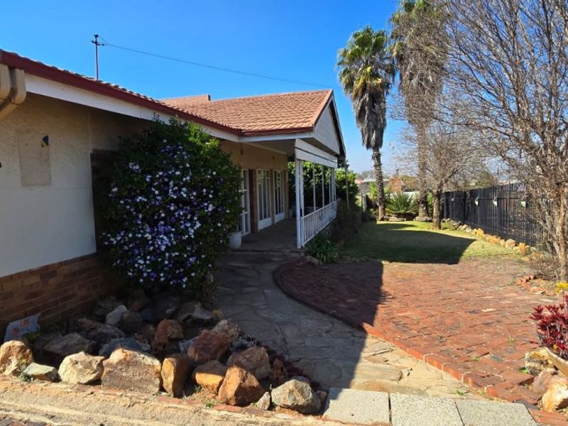 Front elevation of a residential property featuring a covered veranda, brick paved pathway, and established garden with stone landscaping and perimeter fencing.