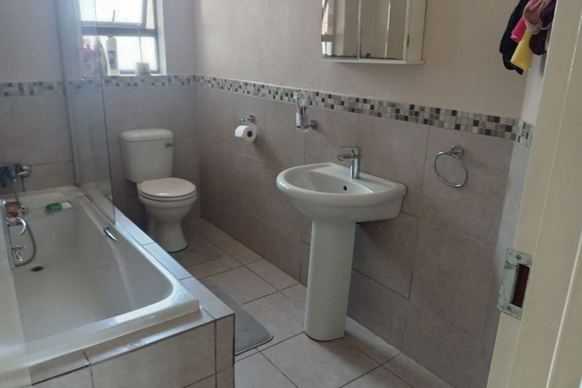 A functional bathroom featuring a pedestal basin, toilet, and a bathtub with a glass shower screen, finished with neutral wall and floor tiles.