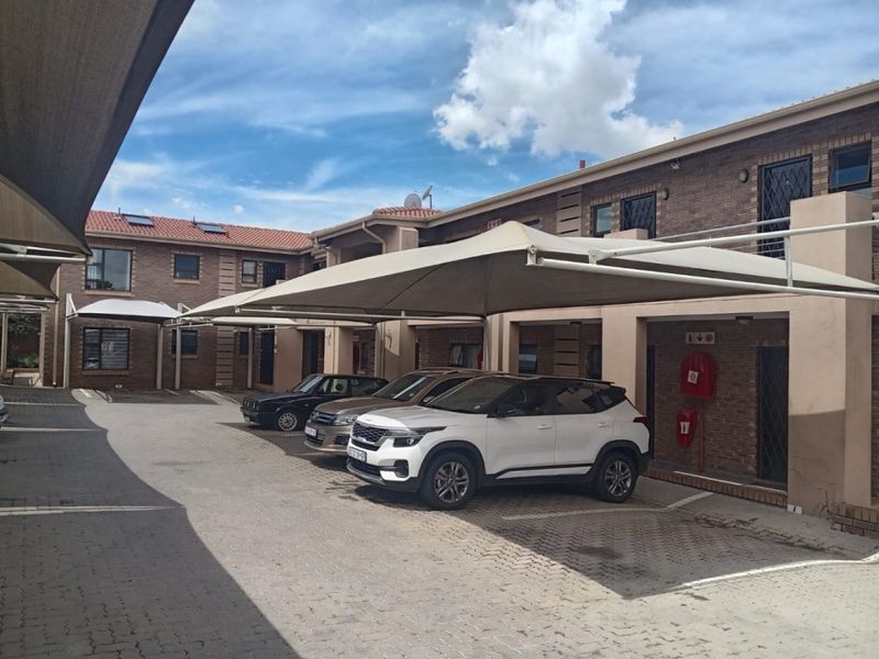Exterior view of an apartment complex parking area featuring paved driveways, covered shade cloth carports, and brick building facades.