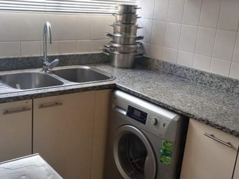 A functional kitchen featuring granite countertops, a double bowl stainless steel sink, tiled splashbacks, and built-in cabinetry with an integrated washing machine.