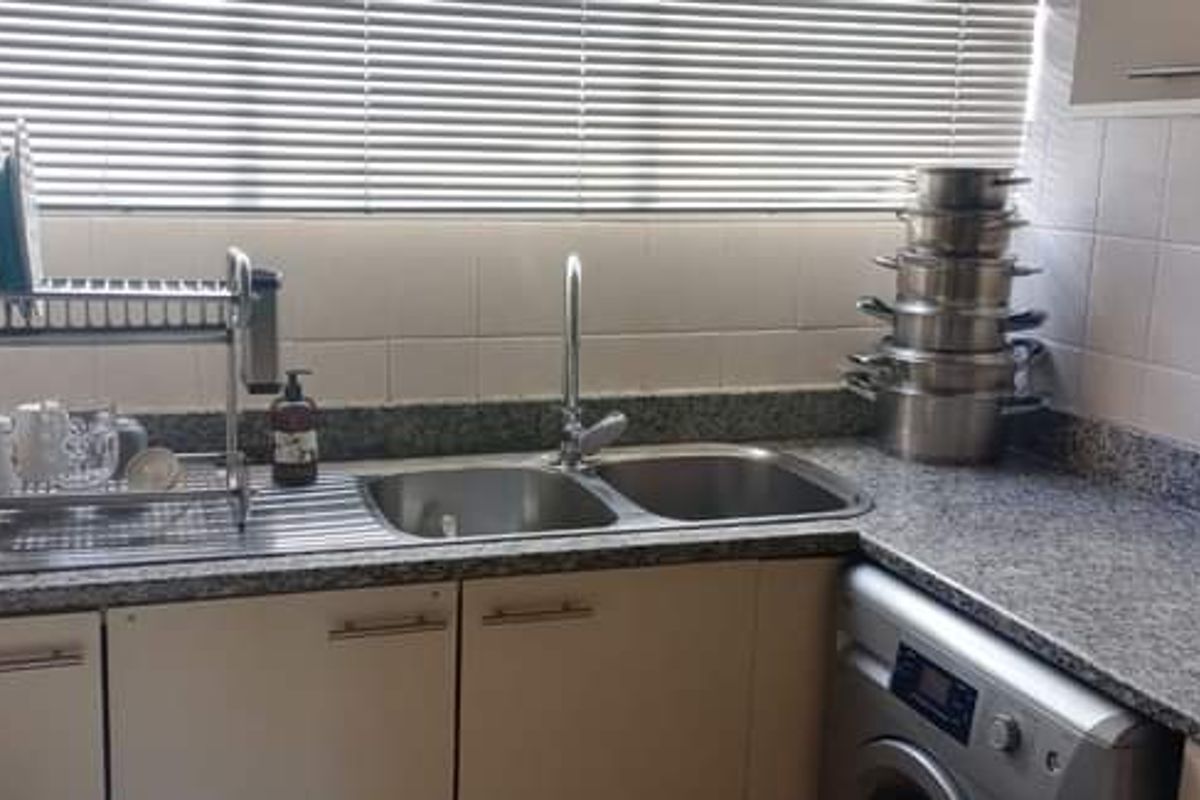 A functional kitchen area featuring granite countertops, a double bowl stainless steel sink, tiled backsplash, and built-in cabinetry with an integrated washing machine.
