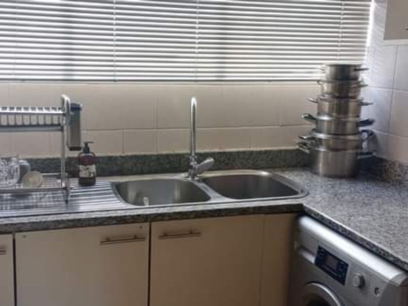 A functional kitchen area featuring granite countertops, a double bowl stainless steel sink, tiled backsplash, and built-in cabinetry with an integrated washing machine.