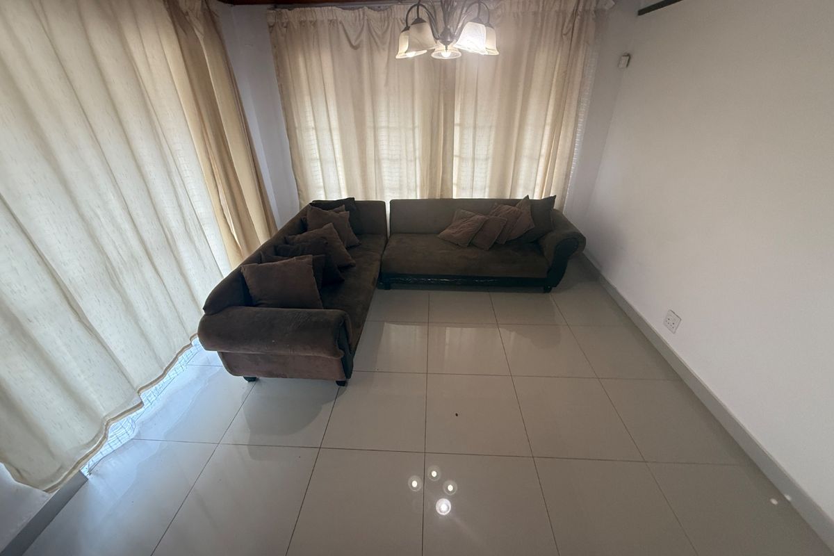 A living room featuring large format floor tiles, a timber ceiling, and a central light fixture, offering a neutral base for interior design.