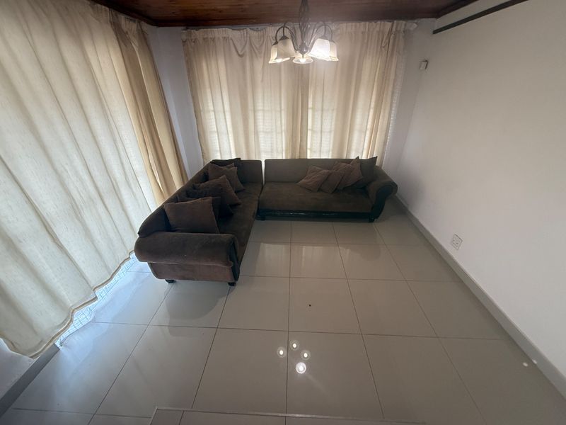 A living room featuring large format floor tiles, a timber ceiling, and a central light fixture, offering a neutral base for interior design.