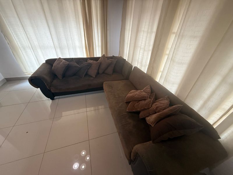 A living room area featuring large windows with curtains and neutral tiled flooring.