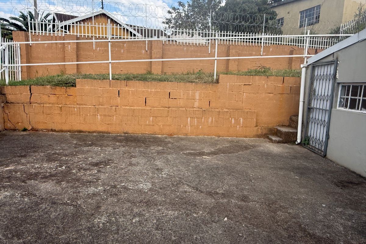 Rear exterior area featuring a concrete paved yard and a tiered retaining wall with security fencing and razor wire.