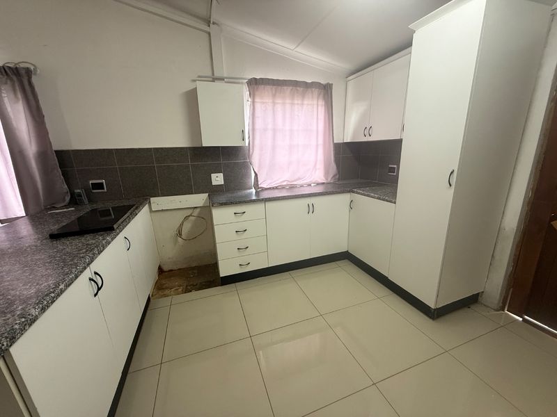 A functional kitchen featuring white cabinetry, granite countertops, tiled backsplash, and ceramic flooring, currently awaiting appliance installation.