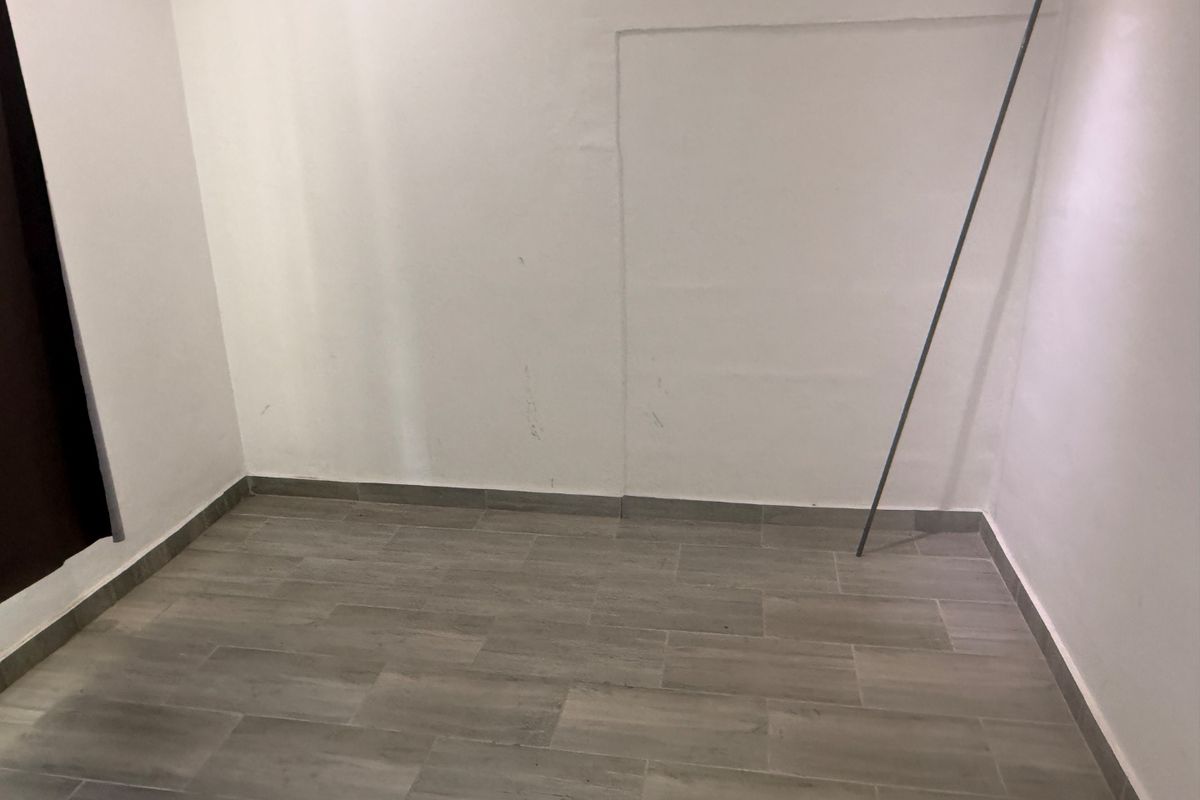 An empty bedroom featuring grey tiled flooring and plain white walls, ready for personalization or staging.