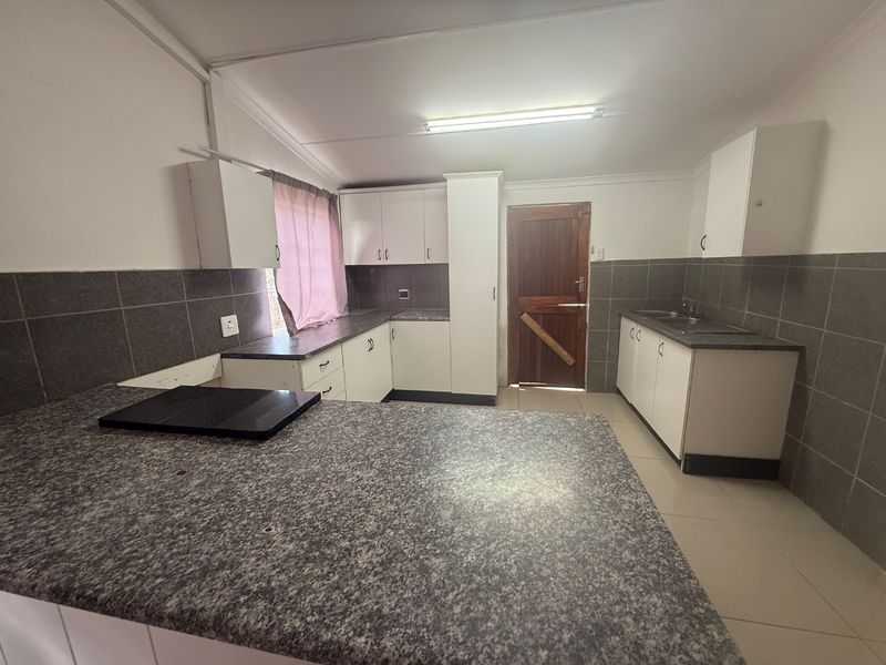 Functional kitchen featuring laminate countertops, ample built-in cabinetry, tiled backsplash, and direct access to the exterior.