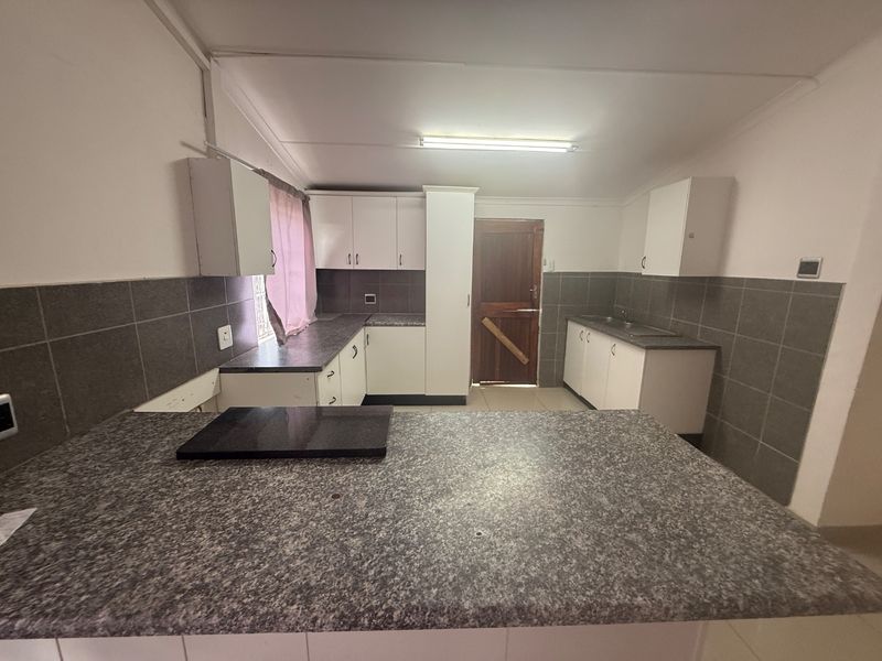 A functional kitchen featuring laminate countertops, ample built-in cabinetry, a double sink, and tiled backsplash, offering a clean and practical workspace.