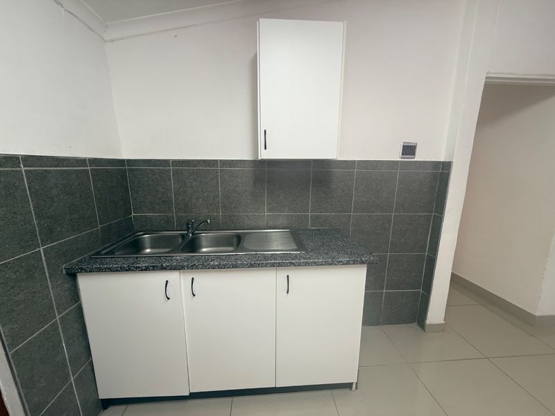 A clean and functional scullery area featuring a double bowl stainless steel sink, granite countertop, and white cabinetry with grey tiled backsplash.