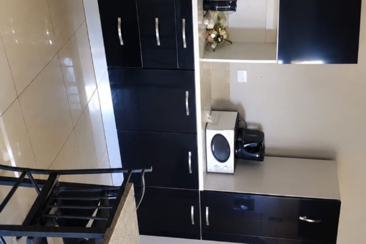 A modern kitchen featuring high-gloss black cabinetry, tiled flooring, and a functional layout with built-in microwave and ample counter space.