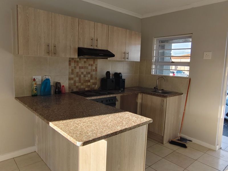 A functional kitchen featuring light wood-look cabinetry, granite-style countertops, a built-in oven with extractor fan, and direct access to the exterior.