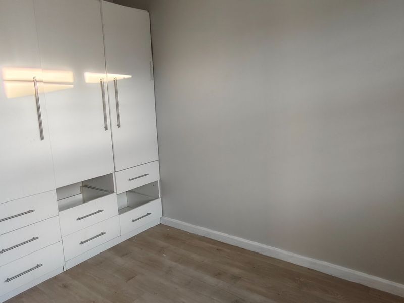A bedroom featuring light-toned laminate flooring and white built-in cupboards with some missing drawer fronts.